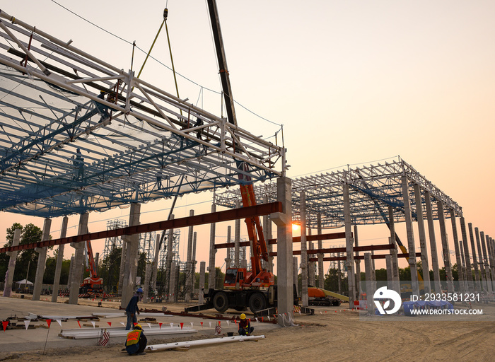 Construction workers are working at height above roof to instrallation accessory steel structure roof truss at construction site factory project during sunset time