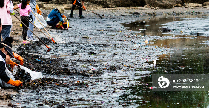 Adult and children volunteers collecting garbage on the sea beach. Beach environment pollution. Tidying up rubbish on beach. People wear orange gloves picking garbage up in to plastic bag.