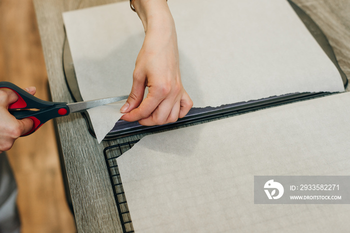 Hand holding up a sheet of baking paper and cut using a pair of scissors.