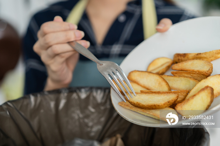 Cholesterol of junk meal is fat meal, asian young household woman scraping, throwing food leftovers into the garbage, trash bin from potato chip, snack in kitchen. Environmentally responsible, ecology