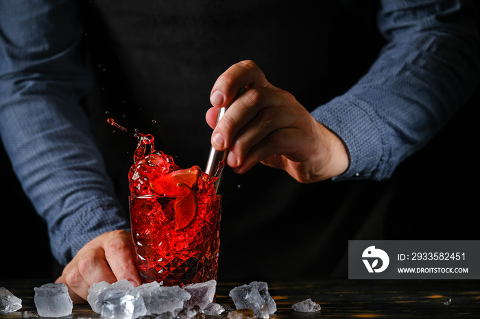 Barman making cocktail with a lot of ice and lime at the bar. Cocktail on black background. Summer cocktail at the nightclub.Red cocktail with ice.