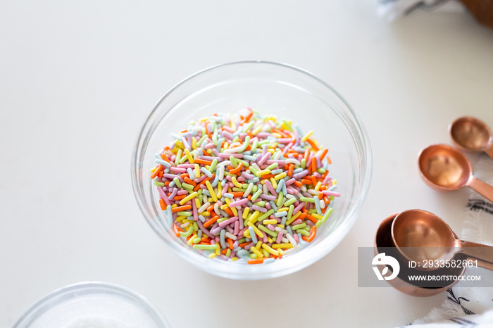 cake ingredients on white background, rainbow sprinkles in bowl