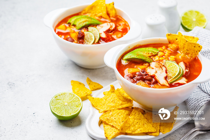 Mexican soup (Chili con carne) with beans, chicken, corn and nachos in white bowls - traditional mexican food.