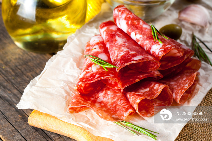 Italian salami with olives and spices on wooden background