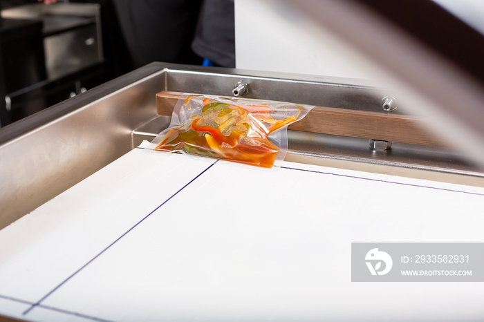 A view looking inside a vacuum packing machine, used in the industry to seal plastic bags of food. A bag of sweet and sour sauce is ready to be sealed.