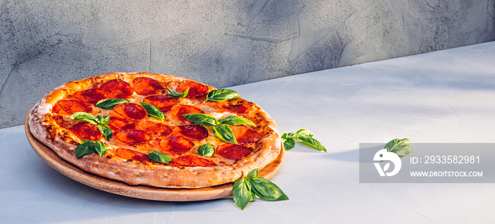 Pepperoni pizza with basil on kitchen table in sunlight