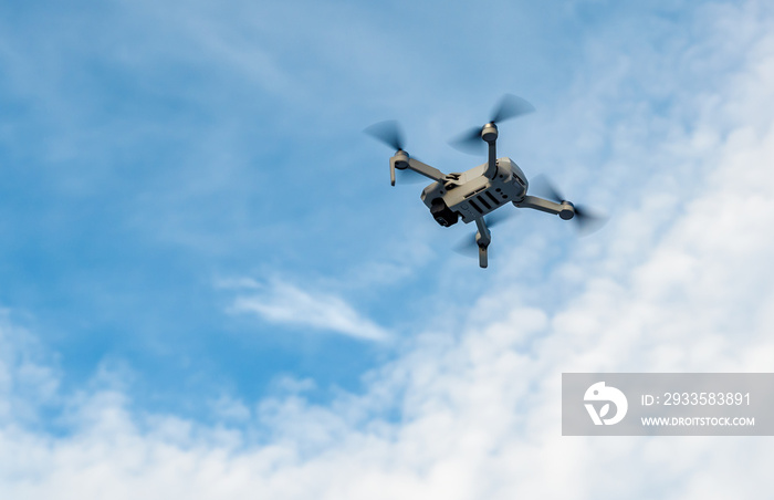 Small drone flying in a cloudy blue sky.