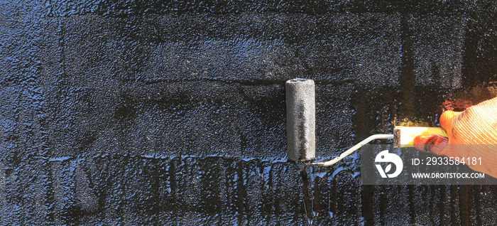 Roofer paints the surface of asphalt bitumen with a roller brush