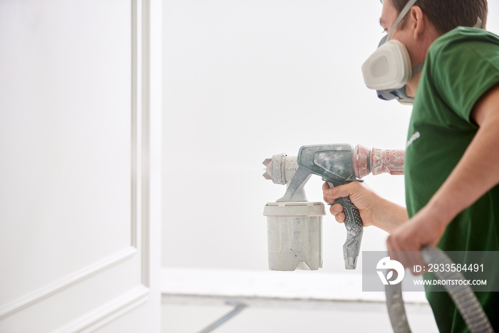 Worker painting wall with spray gun in white color.