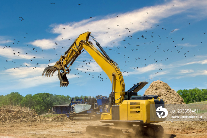 Crane holding and loading roots wood into a chipper shredder and grinding machine with construction zone