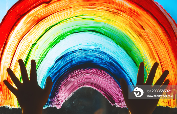 Child hands touch painting rainbow on window.