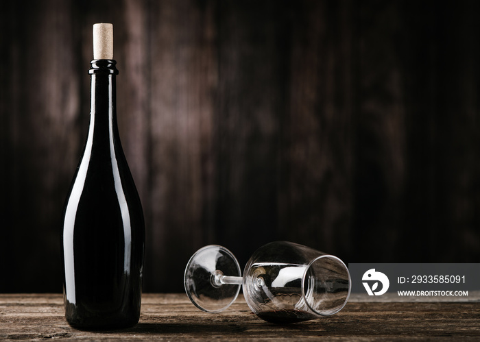 Red wine bottle with empty wine glass on dark wooden table