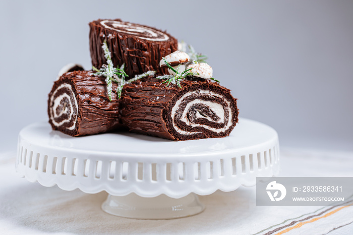 French dessert called Yule log or bûche de Noël with merengue mushrooms and mint leaves on top of chocolate glazing. Placed in front of Christmas tree. Decorated for Christmas Holidays or New year