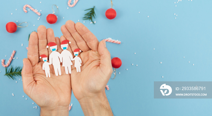 Hands holding a paper-cut family with masks at Christmas. Social distance covid 19. New normality.