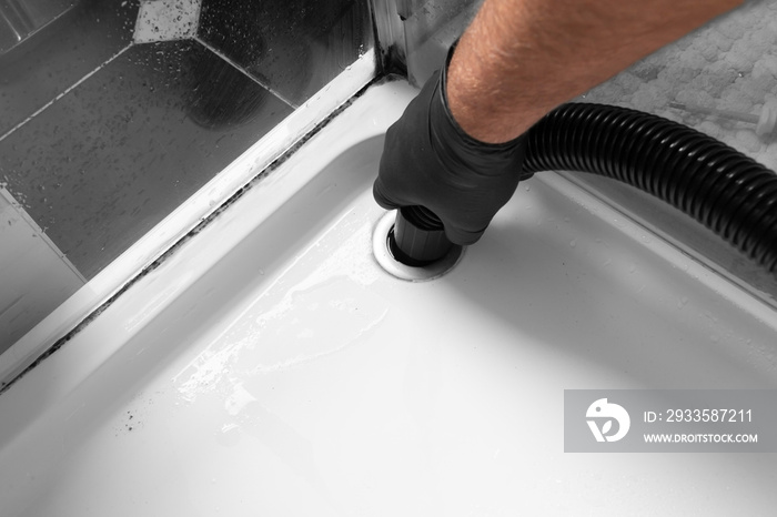 Man unblocking pipes in a bathroom shower cubicle using a hoover. Do it yourself maintenance concept