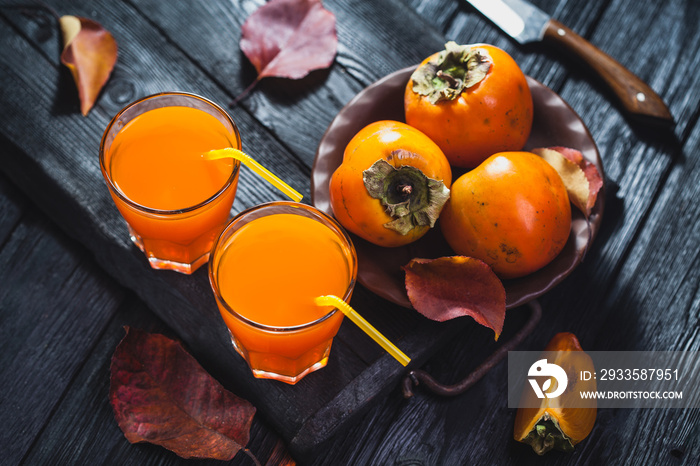 Ripe orange persimmon fruit and persimmon leaves in a brown plate on a black wooden table