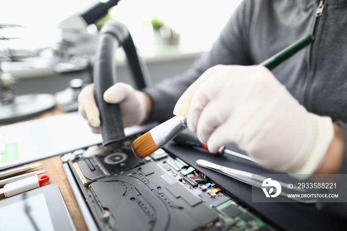 Male chemist in white protective gloves use vacuum cleaner in laptop repair service. Technical prevention of device performance and protection against overheating concept