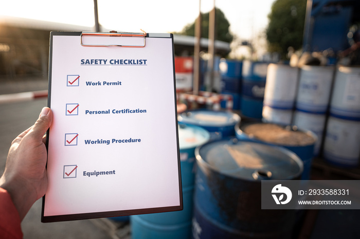 Hand of operation staff is using the safety checklist sheet to verify working condition in chemical storage area (blurred background). Working in unsafe workplace concepts action photo.