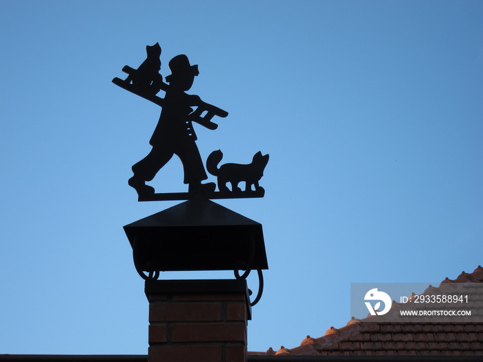 Silhouette of a chimney sweep with cats and stairs to the flue pipe of red brick in front of the blue sky