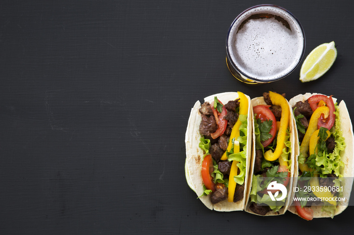 Corn tortillas with beef and vegetables, beer and lime on a black background, top view. Mexican kitchen. Copy space. Flat lay.