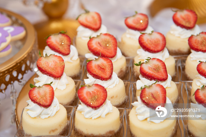 strawberry mini cheesecake in a row. Decorated with cream, a slice of fresh strawberry on top and edible golden glitter.