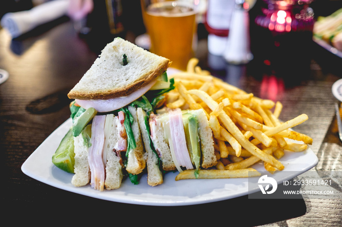 Delicious sandwich of tomato, lettuce, avocado, cheese and ham, and fries in a plate with beer  at Los Angeles, CA