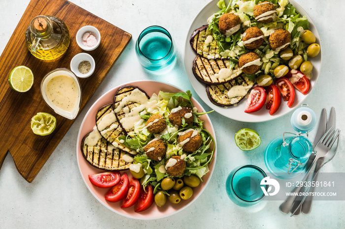 an appetizing dinner or lunch from a salad with tomatoes, grilled eggplants and legume falafel with sesame tahini dressing. Vegan healthy food for the whole family