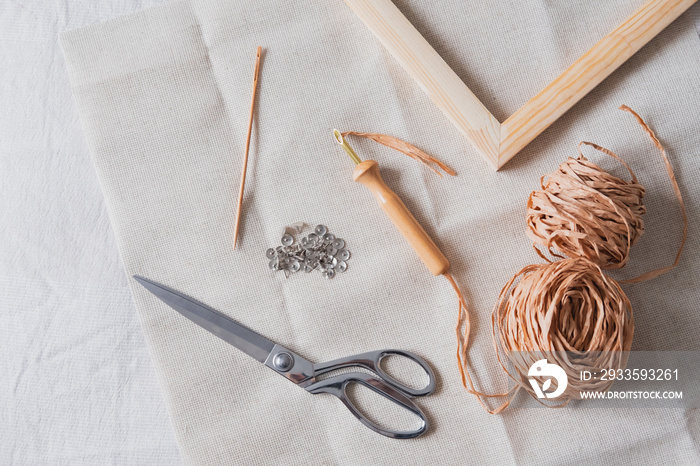 Knitting, handmade, handicraft hobby objects shot from above. Wood frame, macrame threads, needles and scissors in natural linen backdrop