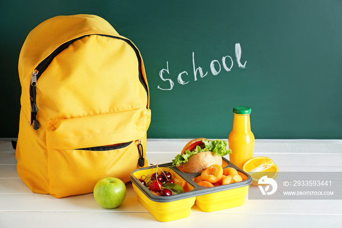 School lunch box with tasty food and backpack on table in classroom