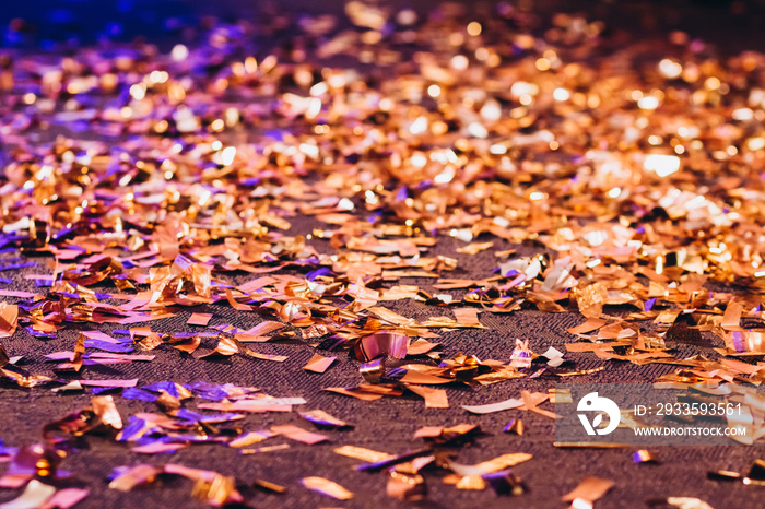 Golden Confetti on a wooden floor reflecting red stage spotlight causing colorful glow