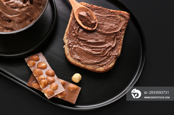 Board of tasty toast with hazelnut butter and chocolate on dark background, closeup