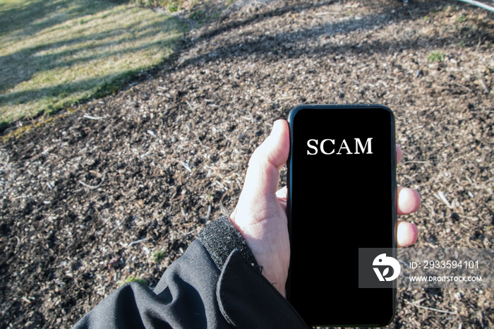 Male Caucasian hand in black jacket outdoors holding smartphone that says call is from spam