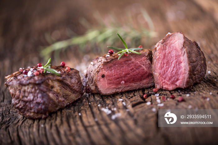 Grilled beef steak with rosemary, salt and pepper on old cutting board. Beef tenderloin steak.