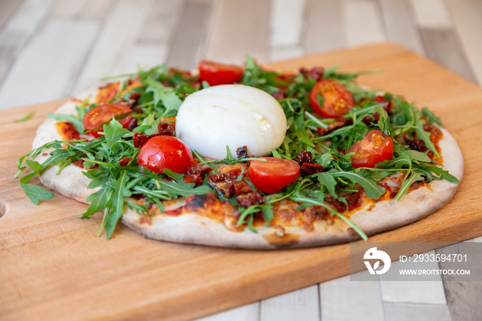 a pizza on a wooden board with cherry tomatoes, arugula, and cheese