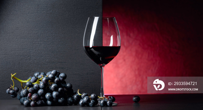 Red wine grapes on a black table and glass of red wine.