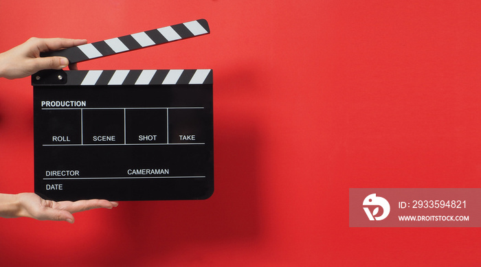 A Hand is holding Black clapper board or movie slate on red background.It used in cinema industry and video production.