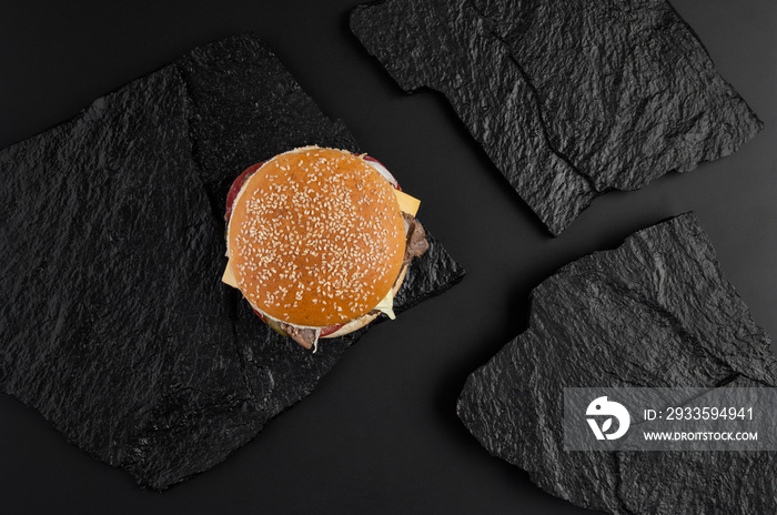 juicy cheeseburger on a background of black stone plates. the view from the top