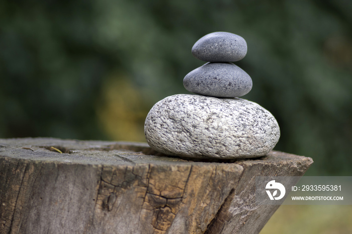 Three zen stones pile on wooden stump, white and grey meditation pebbles tower