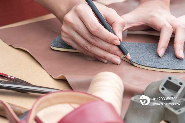 Close up shoemakers’s hands drawing or drafting woman shoes template for cutting leather with tools and accessories on table.