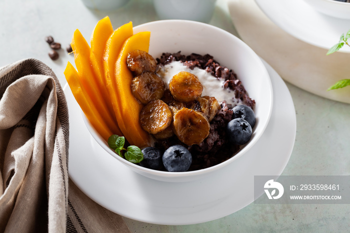 Caribbean sweet breakfast of black rice porridge with coconut milk and mango, fried bananas. Healthy Jamaican cuisine. And coffee