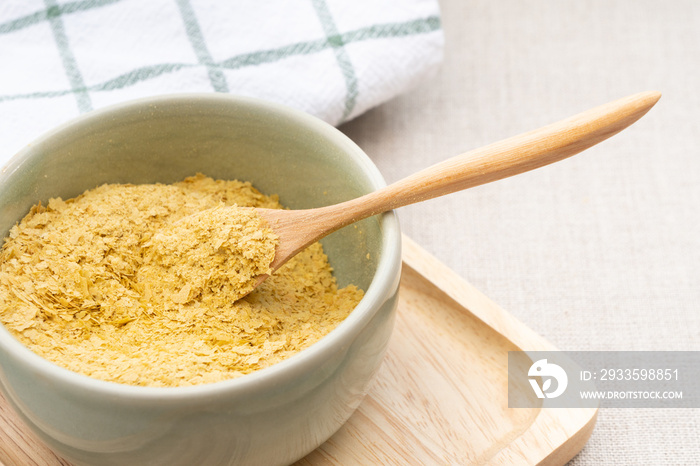 Top view & Closeup, Yellow flakes of nutritional yeast in ceramic bowl and wooden spoon, excellent source of vitamins, minerals, and high-quality protein for plant-based diet / vegan food.