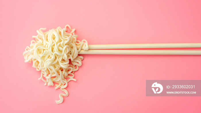 Instant noodles and chopsticks on a pink background.