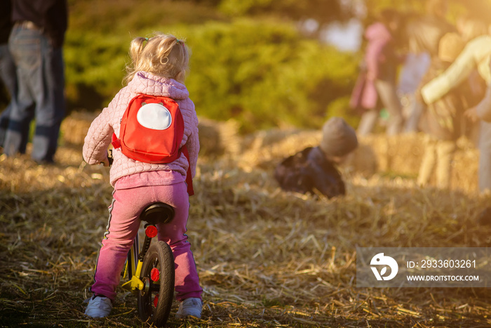 Girl with a red backpack on a kid’s bike in the park