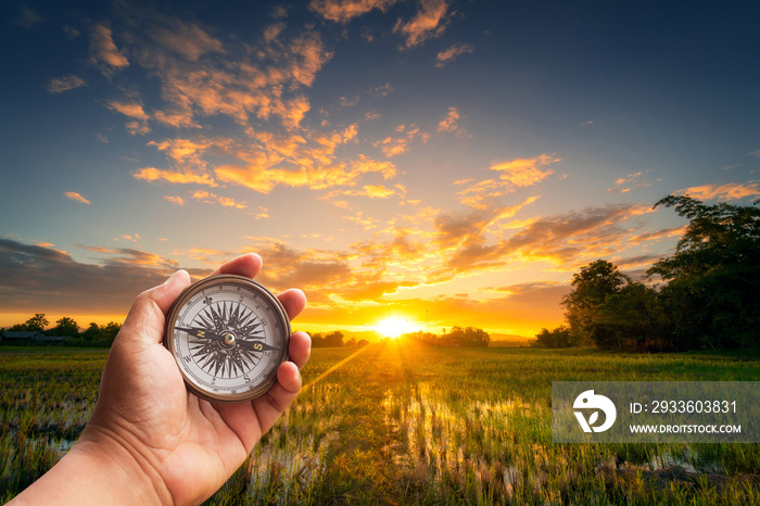 A man holding compass on hand at field and sunset for navigation guide.