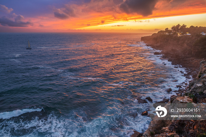 Red colorful sunset and vivid dramatic sky at rocky shore of the Atlantic ocean.