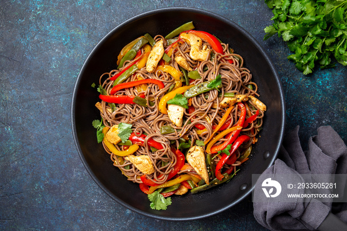 Japanese dish buckwheat soba noodles with chicken and vegetables carrot, bell pepper and green beans in wok on dark blue background