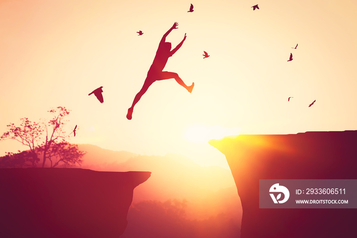 Silhouette man jumping between cliff at top of mountain background with birds flying. Freedom challenge and travel adventure concept.