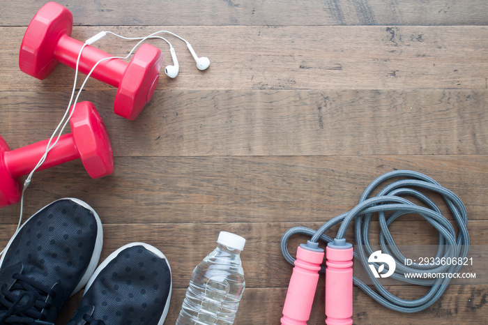 Red dumbbells, sport shoes, bottle of water and jumping rope on wood background with copy space