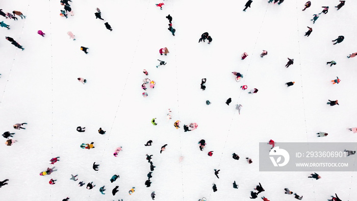 Aerial Drone View Flight Over many people in colorful clothes skating on an open-air ice rink in winter. Ice skating top view. City Park Ice Rink. Winter outdoor activities. Skating sport background