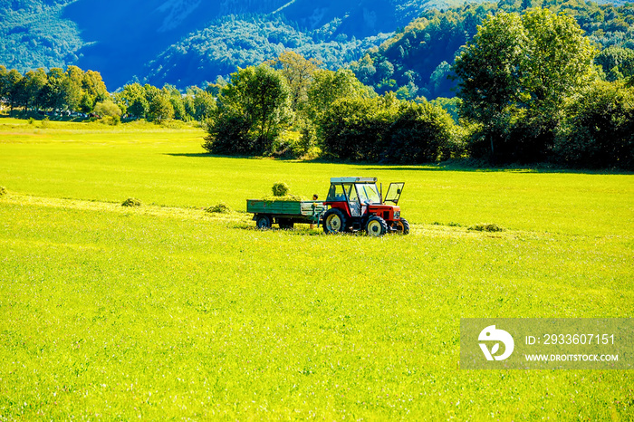 Tractor on green meadow and beautiful Alpine mountains in the background.